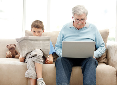 Old man using a laptop with his grand son reading a newspaper - Indoor